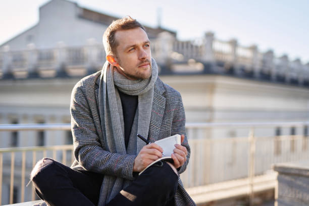 istock Young man sitting and thinking, holding notepad with pen 1293084055