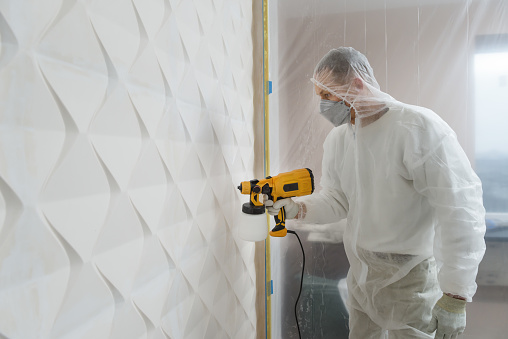 The painter is painting a 3d wall with a spray gun.