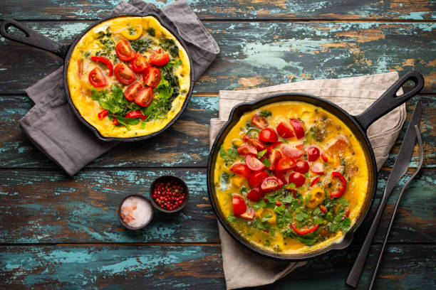 Italian frittata with eggs and vegetables Healthy frittata in two cast iron pans with fried beaten eggs and seasonal vegetables on rustic wooden background. Italian omelette with organic spinach, bell pepper, tomatoes, top view frittata stock pictures, royalty-free photos & images