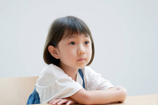 椅子の上で考えているアジアの女の子 - 6歳から7歳 ストックフォトと画像