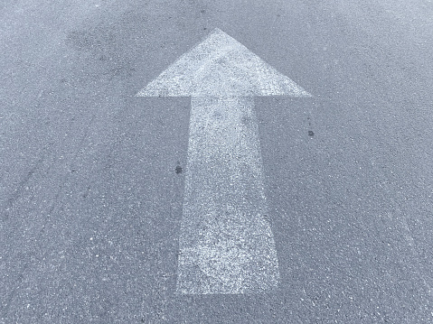 faded white direction directional in or out arrow on asphalt entrance drive or road