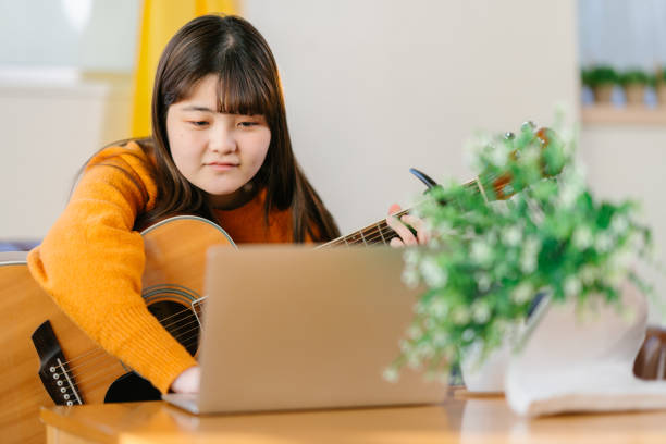 istock Young woman learning playing acoustic guitar via online training classes at home 1293116803