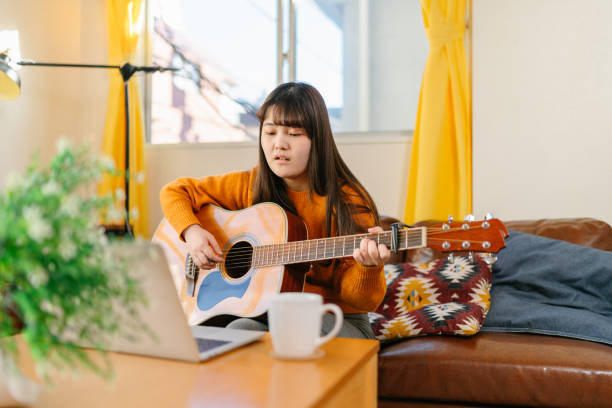 istock Young woman learning playing acoustic guitar via online training classes at home 1293116815