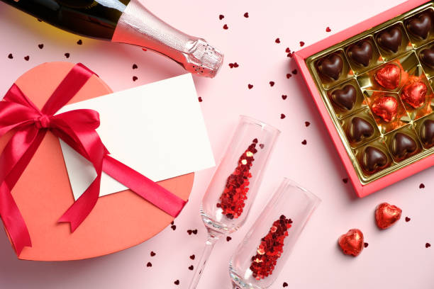 istock Romantic flat lay composition with champagne bottle, glasses, box of chocolates, heart shaped gift box with blank paper greeting card on pink background. Happy Valentines Day concept. 1293123861