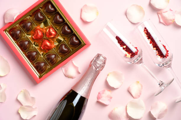 romantyczna kolacja. pudełko czekoladek, butelka szampana i kieliszki z konfetti na różowym tle ozdobione płatkami róż. walentynki uroczystości koncepcji. - champagne pink luxury table zdjęcia i obrazy z banku zdjęć