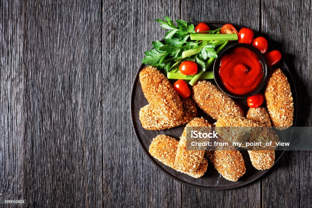 Deep-fried italian suppli al telefono rice croquettes stuffed with mozzarella Deep-fried italian suppli al telefono rice croquettes stuffed with mozzarella served on a black plate with celery stalks, tomatoes, and ketchup on a dark wooden table, top view, copy space Croquette Stock Photo
