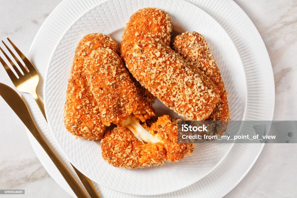 Deep-fried italian suppli al telefono rice croquettes stuffed with mozzarella Italian snack suppli al telefono or rice croquettes stuffed with mozzarella cheese served on a white plate on a light marble background, top view, close-up Suppli Al Telefono Stock Photo
