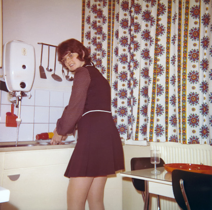 Vintage 1972 image of a young woman with mini skirt doing the dishes in the kitchen.