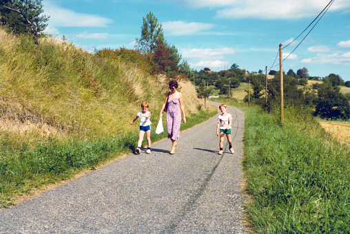 Vintage early 1980s image of a mother walking with her two children on a road in a summer landscape