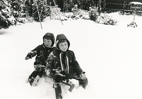 Vintage early 1980s image of two brothers on a sleigh in a wintery snowy garden.