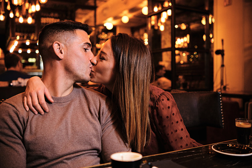 Portrait of lovely young couple kissing while enjoying a date at restaurant. Couple celebrating valentine's day.