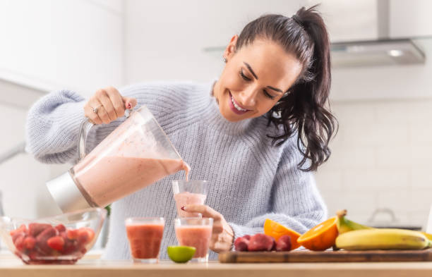 la mujer vierte el batido de frutas en tazas en una cocina. - healthy eating fruit drink juice fotografías e imágenes de stock