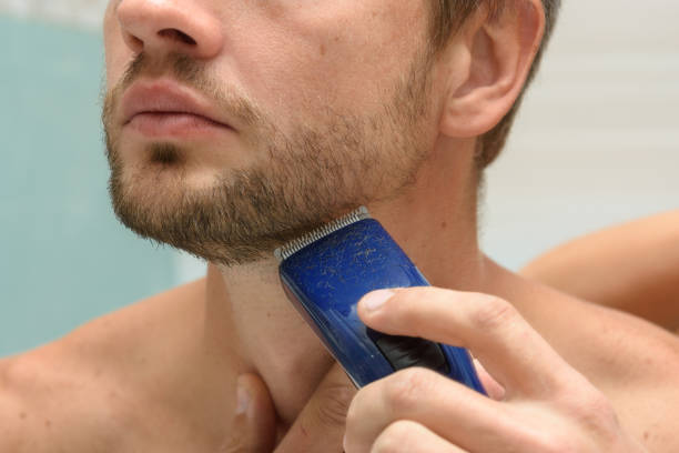 A man cuts a beard on his face with a hair clipper, close-up