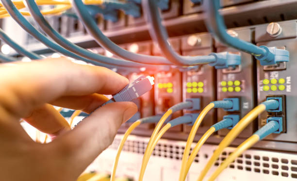 mano con cables de red de fibra conectados a servidores en un centro de datos - fiber optic computer network communication blue fotografías e imágenes de stock