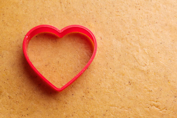 Close-up of woman baker's hands using dough cutter on dough to prepare shaped cookies