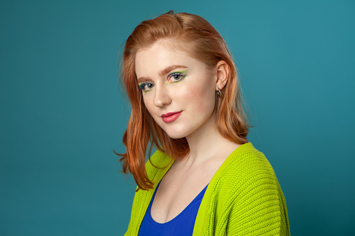 Close-up studio portrait of 19 year old red-haired woman with bright make-up on blue background