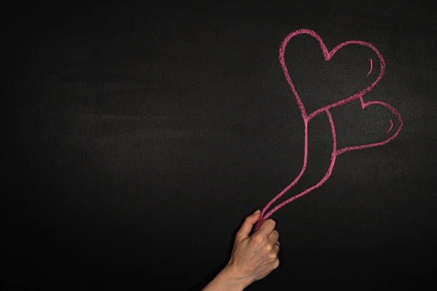 istock Hand holds two heart shaped balloons on a blackboard 1293183363