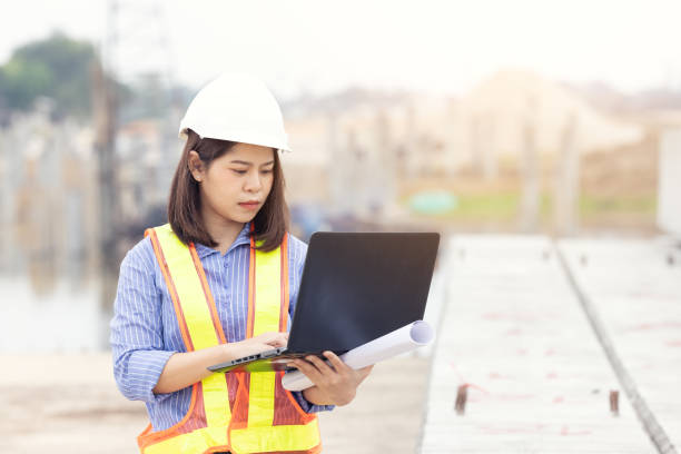 istock Beautiful Asian female engineer in white safety hard hat using laptop computer notebook doing job at construction site outside office. Idea for modern working woman. 1293188120