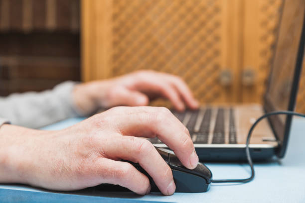 Hands using a laptop The hands of an unknown person using a laptop, moving the cursor with the mouse and typing with the keyboard, on a blue table. smart office stock pictures, royalty-free photos & images