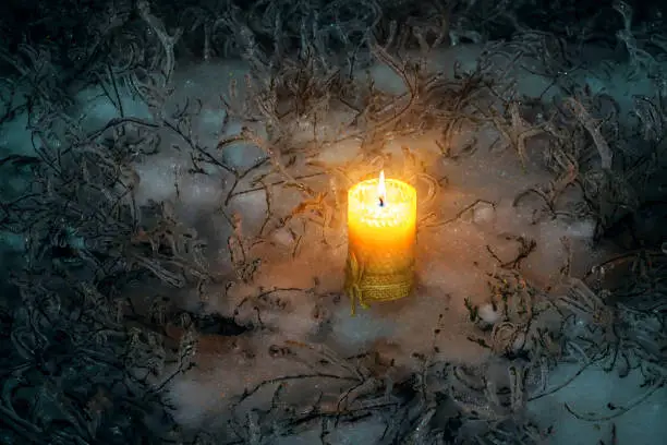 Photo of Christmas burning candle standing on icy snow surrounded by icy grass. Lonely candle in the winter outside at night.