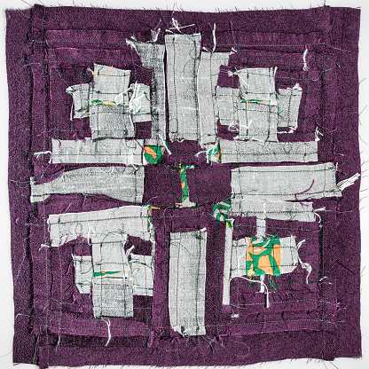 wrong side of stitched detail of patchwork cloth from silver and purple fabrics on white background