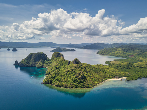 Coastal Drone Panorama View from Vigan Island - Snake Island along Pagauanen Island Coast under blue summer cloudscape. View towards sandy beaches and typical El Nido Islets, Hill Range and Karst Rock Formations. Dibuluan Island in the panorama background. Vigan Island - Snake Island, Pagauanen Coast and Beaches, Mimaropa, El Nido, Palawan, Philippines, Southeast Asia, Asia