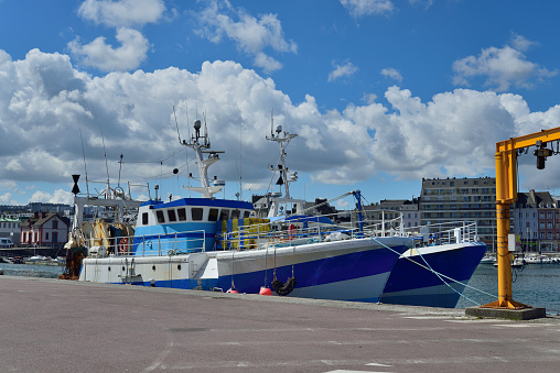 Two commercial fishing trawlers with lobster traps lashed down moored in the Cherbourg harbor on a beautiful spring day with a nice cloudscape of cumulus clouds in the background