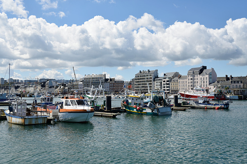 A large collection of commercial fishing boats moored in the Cherbourg, France harbor with the city skyline and buildings in the background