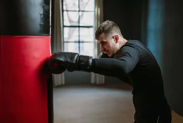 Photo of A young athletic man is hitting a boxing bag. Boxer practicing punches in the ring. The athlete strikes with a punching bag. 4k video