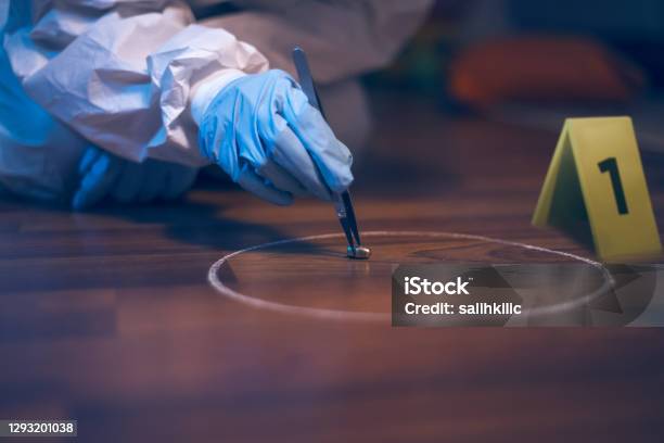 Forensic Scientist Working At The Crime Scene A 9mm Bullet Collecting With Tweezers On The Floor Stock Photo - Download Image Now