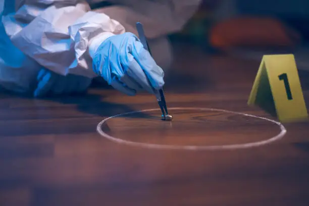 Photo of Forensic scientist working at the crime scene. A 9mm bullet collecting with tweezers on the floor.