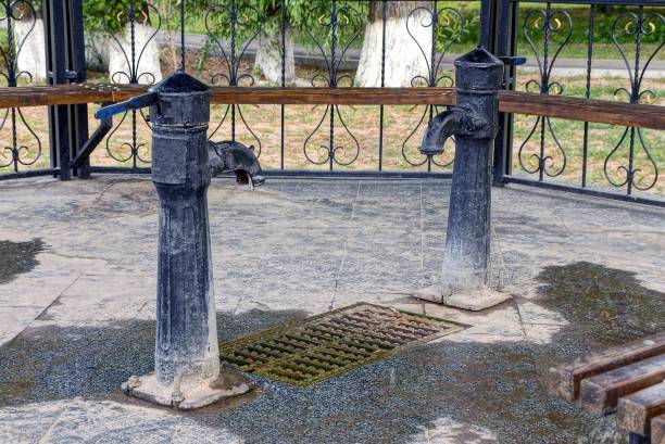 two black iron water pump taps stand on a gray sidewalk in an open gazebo