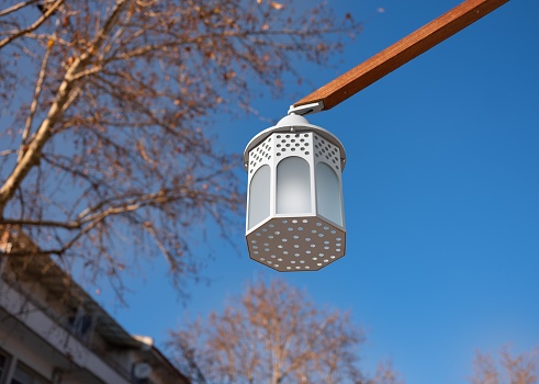Old fashioned street lighting lamp hanging on a wooden pole with autumn trees and blue sky background