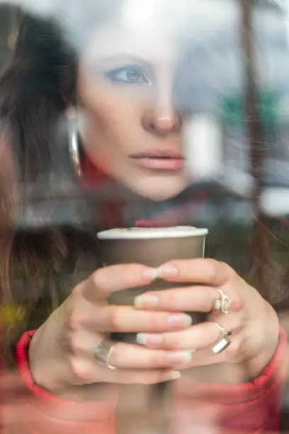 Photo of face of young and beautiful latin woman, having a cup of coffee, uses makeup, glasses and red sweater, photo in the day