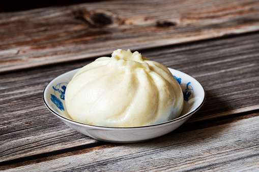 A steamed stuffed bun in a small ceramic plate on rustic wooden table. Closeup and macro.