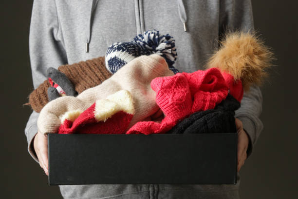 femmes volontaires retenant la boîte de donation avec les vêtements hivernaux chauds de laine, les chapeaux, les chaussettes, les gants... - vêtement chaud photos et images de collection