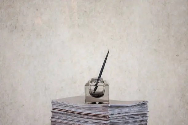 Picture of a dip pen in an inkwell on display on a pile of paper. A dip pen or nib pen or pen nib usually consists of a metal nib with capillary channels like those of fountain pen nibs, mounted in a handle or holder, often made of wood.