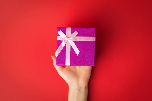 istock Left female hand with a gift box on a red background. 1293247323
