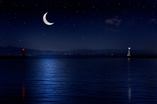 Crescent moon rising over the sea and the lighthouse with copy space.
