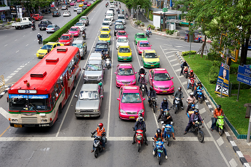 Colorful cars, taxis and motorcycles stopping at an intersection during rush hour in downtown Bangkok City, Asia