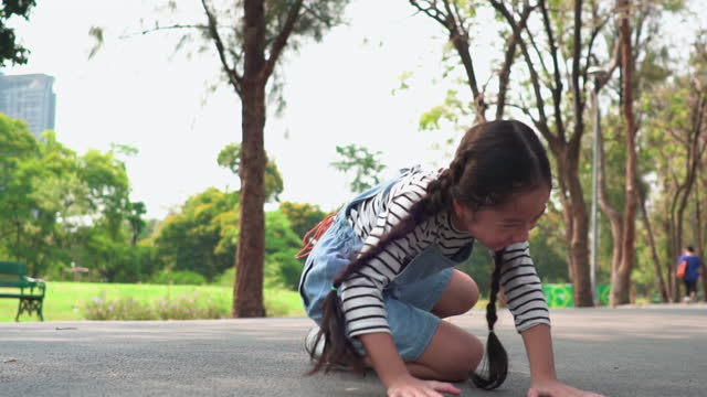 Slow-motion view of a Southeast Asian teenage girl in the park try to do somersault or upside down on the footpath, but she's failed by fall with feeling positive emotion and happiness of smiling. Cheerful child playing at weekend activities.