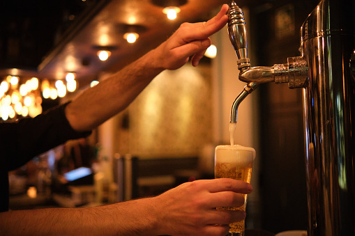 Close-up of a barman pouring beer in glass from beer tap at bar or pub. Metallic equipment for bars and breweries. Craft beer.