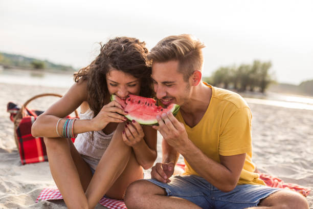 istock Couple having fun while sharing a slice of watermelon during a beach picnic 1293281073