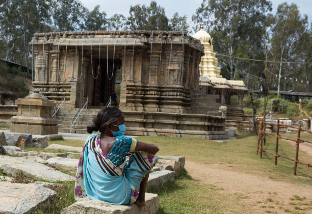 una povera signora senza tetto è vista seduta di fronte al tempio shiva. - indian ethnicity traditional culture architecture karnataka foto e immagini stock