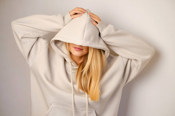 Young beautiful girl in a white hoodie posing. Warm oversized hoodie with an hood. Stylish trendy hipster bow. Trying on clothes in a store. Youth subculture. Fashion clothing advertising stock photo