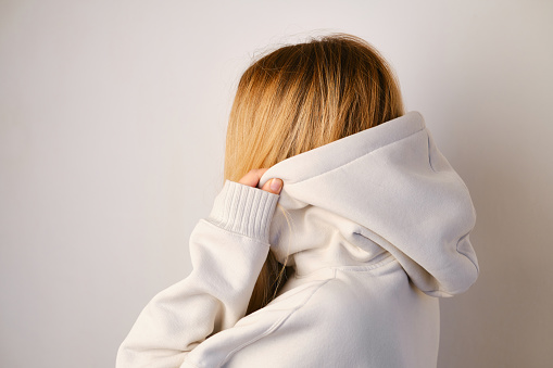 Young beautiful girl in a white hoodie posing. Warm oversized hoodie with an hood. Stylish trendy hipster bow. Trying on clothes in a store. Youth subculture. Fashion clothing advertising