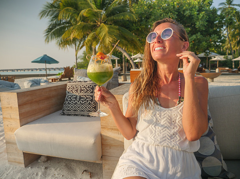 Woman on tropical beach relaxing with cocktail and enjoying sunset