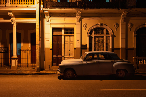 Vintage car parked on a quiet residential street in the historic center of Cienfuegos, Cuba at night. Cienfuegos is well-known for its colonial style buildings, and its city center has been designated an UNESCO World Heritage site.