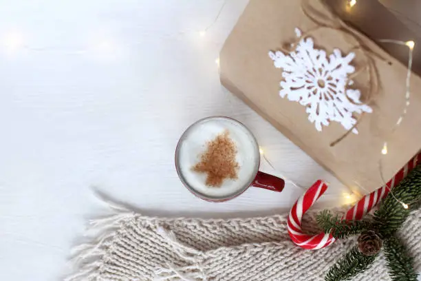 coffee with a picture of a Christmas tree on a table with a scarf, a gift and a garland, top view