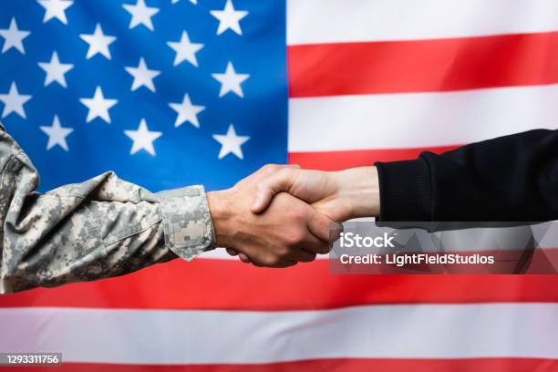 Cropped View Of Soldier Shaking Hand With Civilian Man Near American Flag On Blurred Background Stock Photo - Download Image Now